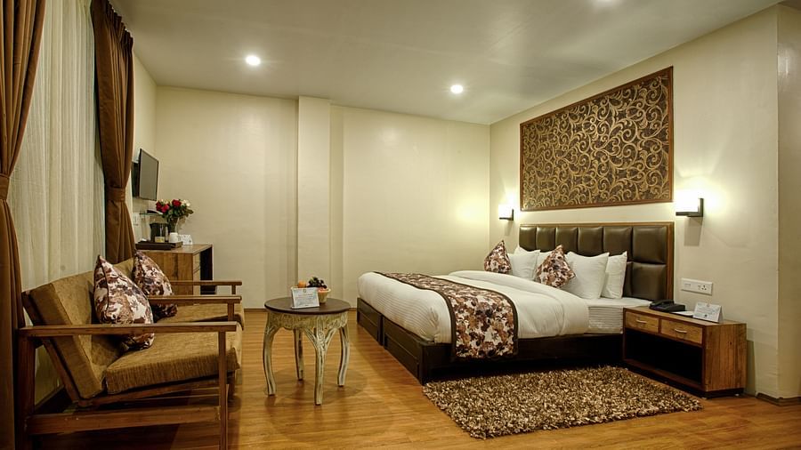 Spacious suite at Voyage The Aryan Regency featuring decorative wall panel, seating area, modern amenities, and warm golden curtains