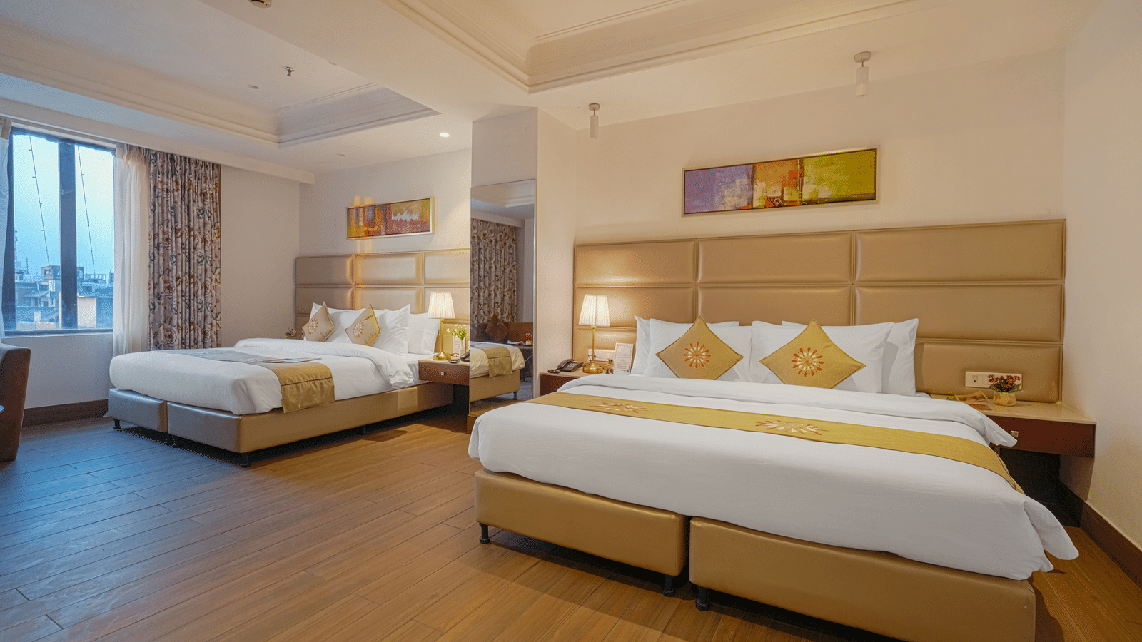A wide-angle view of a hotel room with two large beds, bright lighting, and abstract artwork above the headboard at BluSalzz Select City Centre, Amritsar.