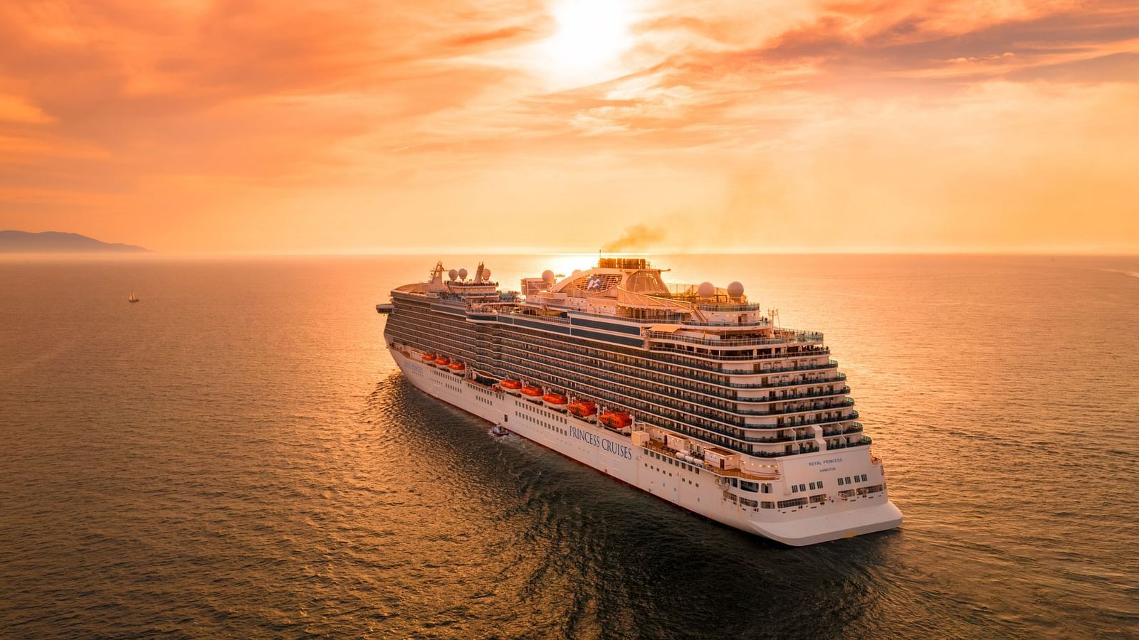a cruise ship floating on a waterbody with the sun setting in the background and the sky showing different hues of orange