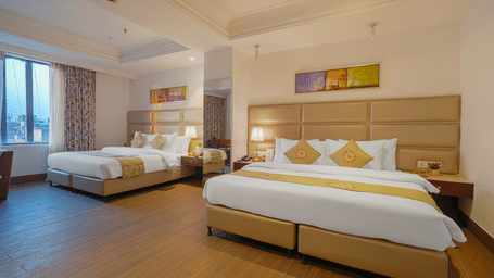 A wide-angle view of a hotel room with two large beds, bright lighting, and abstract artwork above the headboard at BluSalzz Select City Centre, Amritsar.