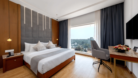A bedroom with a king size bed, a wooden desk with an office chair, and a large window overlooking trees at Tiara by MPS.
