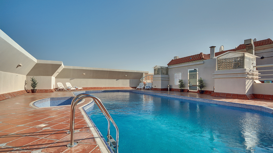 An outdoor swimming pool with blue water is surrounded by terracotta tiles under a clear, sunny sky - Al Manar Grand Hotel Apartment, Bur Dubai
