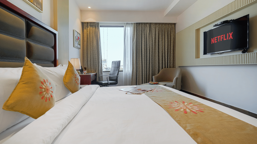 A hotel room featuring a large bed, a wall-mounted television, and a panoramic view of the city through a window at BluSalzz Select City Centre, Amritsar.