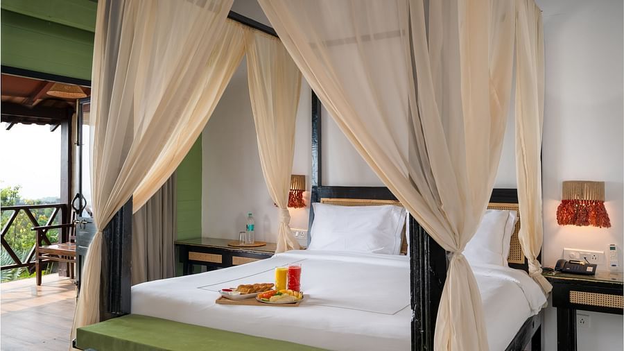 A chic room with flared curtains decorating the large wooden bed frame, placed in a room with a balcony