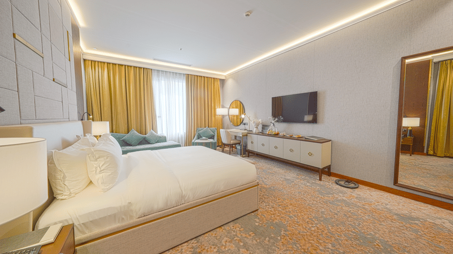 Side view of the Junior Suite with it's plush double bed in the foreground, and seating area placed near closed curtains in the background.