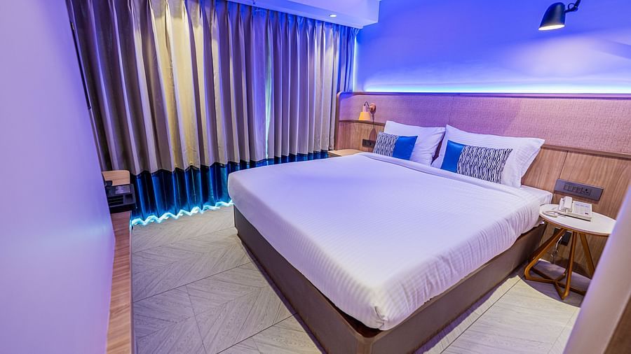 A spacious room at Indie Stays Mumbai International Airport with a diagonal view features a large bed, a bedside table, and curtains fully drawn closed.