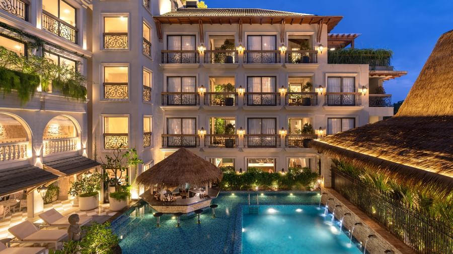 A beautiful swimming pool surrounding by the buildings of The Evren, Vagator, illuminated by exterior lighting during the evening.