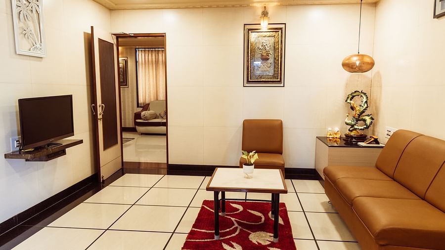 full view image of the living room of the grand suite featuring a brown coloured couch facing towards the television at The Grand Krishna Rooms, Bengaluru