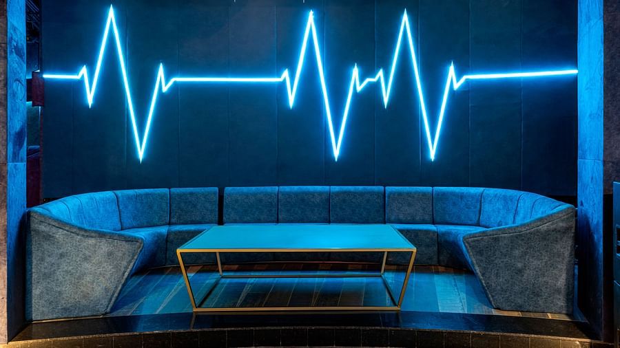 Verve with blue neon light in the shape of a heartbeat line on the wall, with curved seating and a small table at The Qualia Resort Club & Brewery, Udaipur.