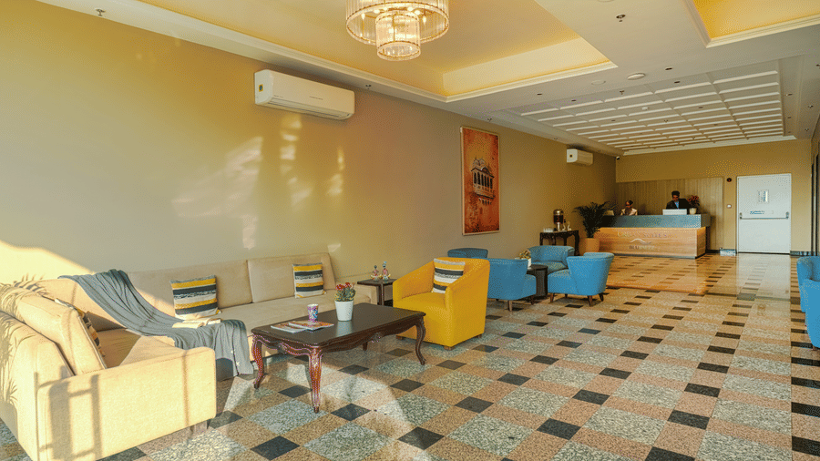 The brightly lit reception at Urban Suites by BluSalzz, Jaipur, with a tiled floor, featuring seating arrangements, a low table, and an air-conditioning unit on the wall.