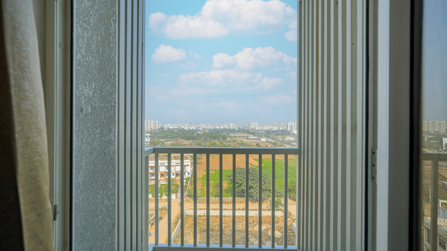 A balcony of a room at Urban Suites by BluSalzz, Jaipur, showing a bright, sunny landscape with buildings and trees in the distance.