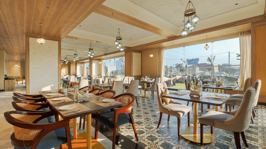 A dining space at Urban Rasoi at Urban Suites by BluSalzz, Jaipur, showing multiple set tables and a outdoor vision.