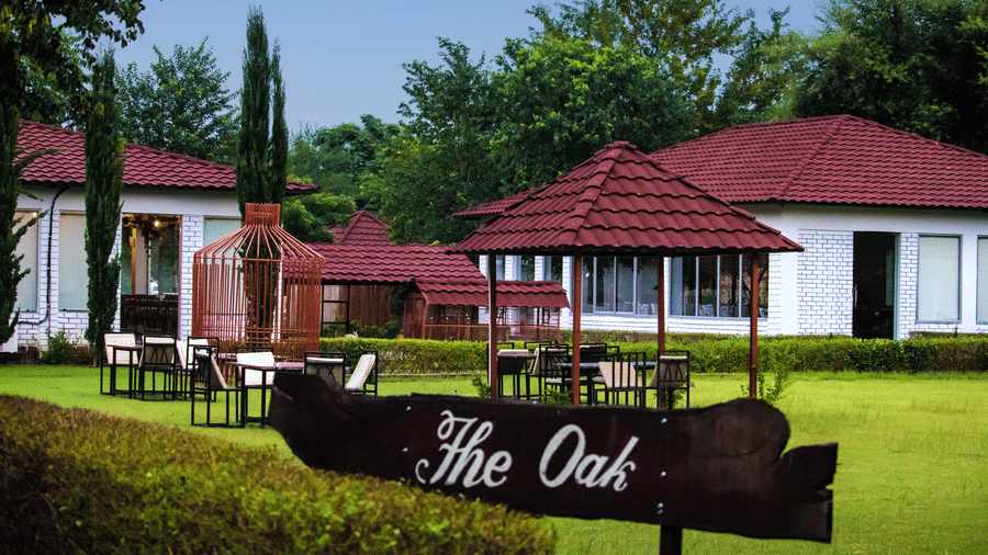 The Oak' signboard with cottages behind at Valley by Grassfield, a resort in Jaipur.