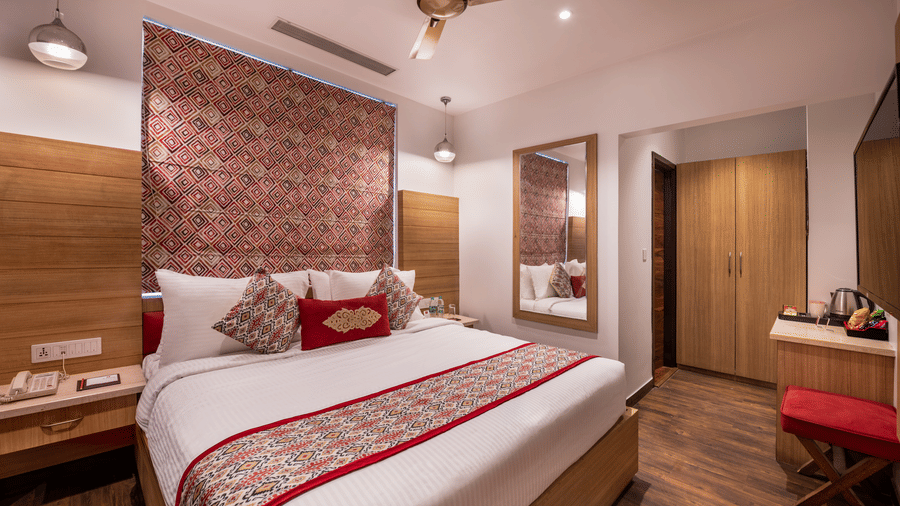 View of a Deluxe Room at Lords Inn Amritsar with a king bed, textured wall panel, wooden flooring, ceiling fan, and warm ambient lighting.