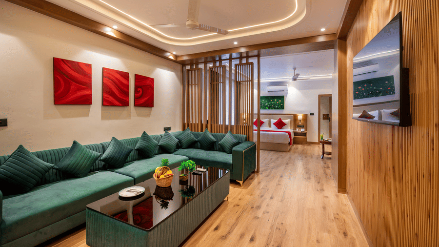 A spacious suite living area at Lords Inn Katra featuring a long corner sofa, a central coffee table, and a television fixed on a wooden wall.