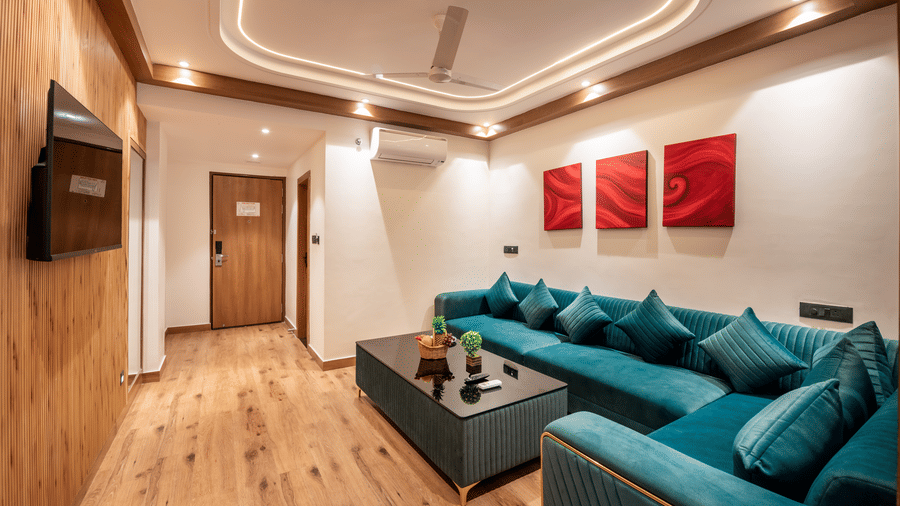 A luxury suite living room at Lords Inn Katra featuring a large sectional sofa, a low coffee table, and 3 framed artworks hanging on the wall.