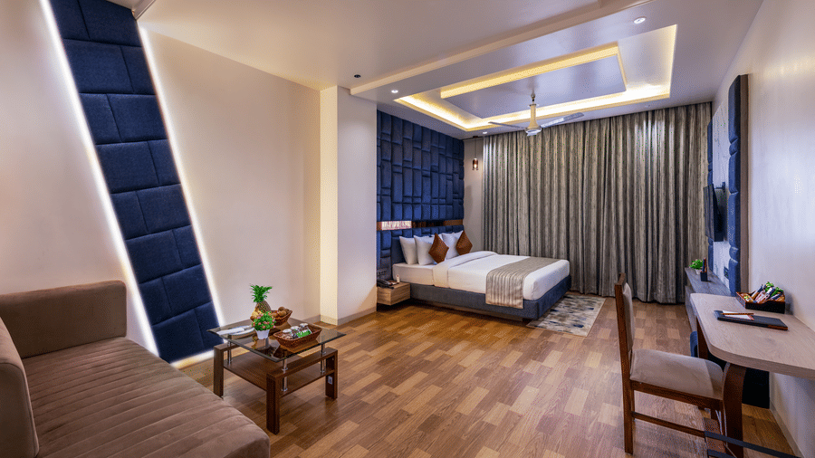 Elegant room at Lords Inn Sangam, Bhopal featuring a bed, blue accent wall, seating table with chairs, and rich wooden flooring.