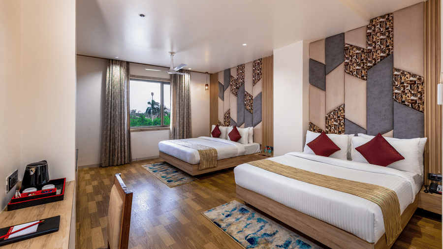 Bright room at Lords Inn Sangam, Bhopal featuring twin beds with patterned headboards, natural light from windows, and wooden flooring.