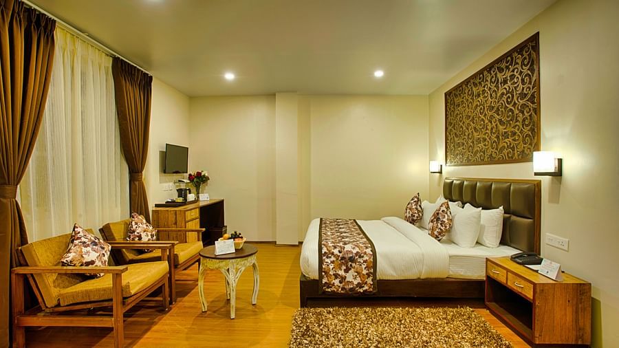 a luxurious suite room with modern amenities and wooden flooring and pristine white walls for a cosy stay - side angle view of lobby area with green-yellow colour furniture and curtained windows behind the couch - the aryan regency