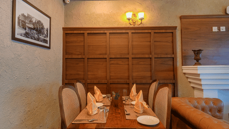 The well-lit Cafe Blusalzz, with walls, a wooden table, chairs, a cupboard, a wall-mounted light fixture, and a framed picture on the wall at BluSalzz Terrah Hills Resort, Dalhousie.