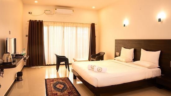 A deluxe ac room with a tv opposite a double bed at Mastiff Select Terrain, Dandel. The room also features a fan, a seating area with two chairs and a centre table, and a large window