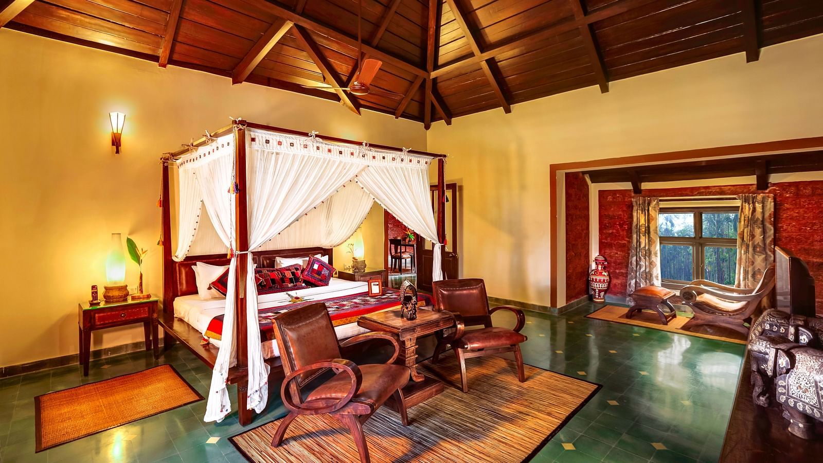 An image of a bedroom with poster bed, some chairs, and a dressing table - Hoysala Village Resort, Hassan