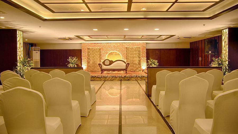 Elegant indoor banquet hall set up with rows of white chairs facing a golden stage backdrop at Voyage Milestone Hotel and Banquet Siliguri