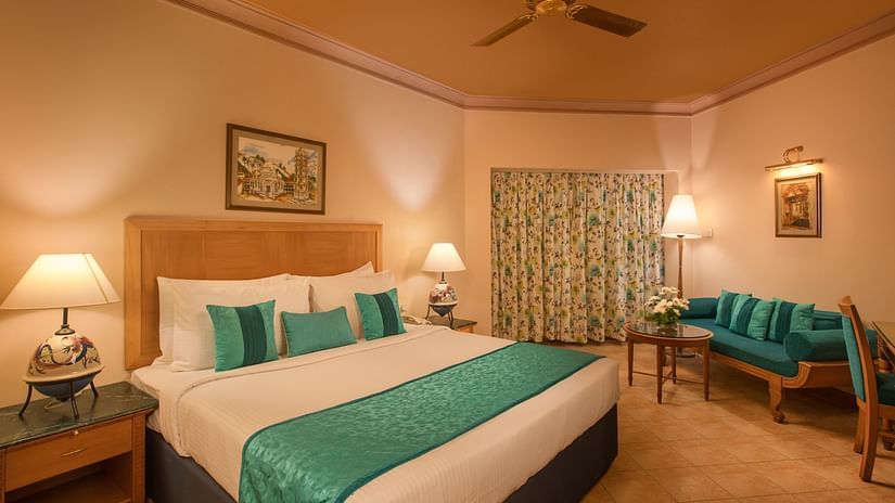 An image of the Deluxe Room with king size bed, bed side table, lamps, sofa set and other amenities at Kenilworth Resort and Spa
