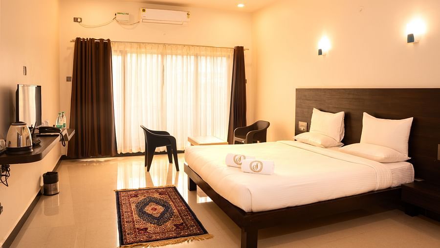 A deluxe ac room with a tv opposite a double bed at Mastiff Select Terrain, Dandel. The room also features a fan, a seating area with two chairs and a centre table, and a large window