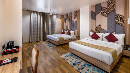 Elegant room at Lords Inn Sangam, Bhopal featuring twin beds with red accent pillows, patterned headboard, and warm wooden flooring.