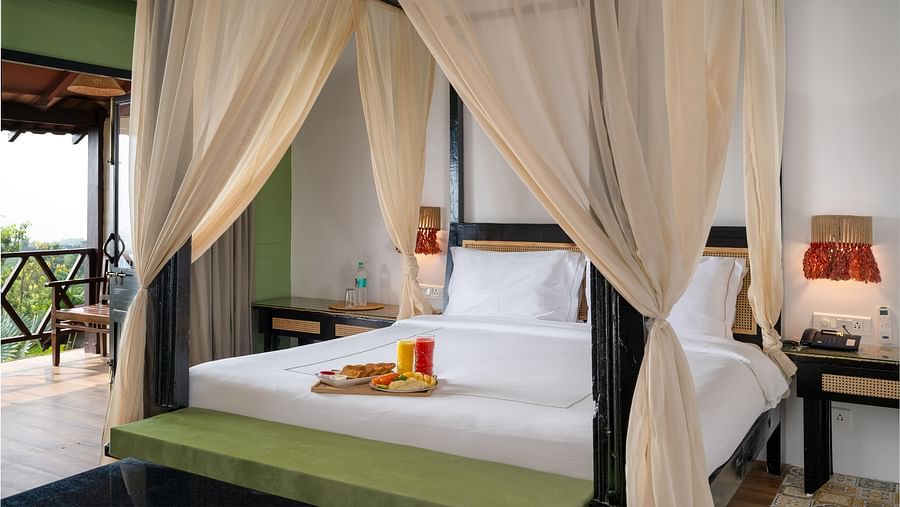 A chic room with flared curtains decorating the large wooden bed frame, placed in a room with a balcony