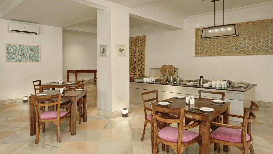 Lobby restaurant at Fateh Safari Resort, Kumbhalgarh featuring sets of tables and chairs and a kitchen counter where several utensils are kept.