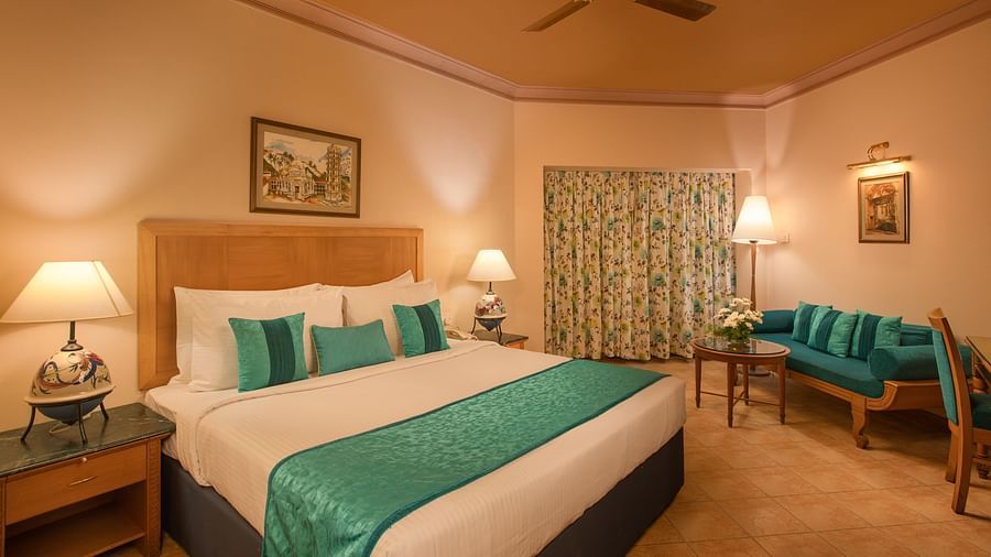An image of the Deluxe Room with king size bed, bed side table, lamps, sofa set and other amenities at Kenilworth Resort and Spa