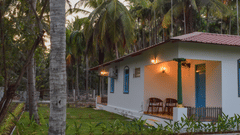 A white resort cottage with a red roof and blue window frames, surrounded by palm trees and green lawns - Ibex Resorts, Coimbatore (Kakarla)