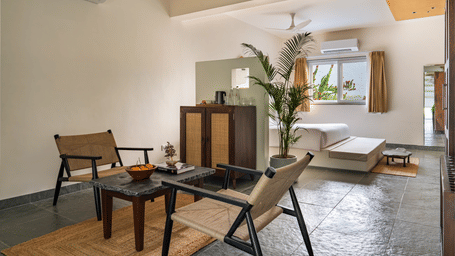 Spacious suite at Vihara, a luxury resort in Udaipur, featuring a plush king bed, comfortable lounge seating, a wooden dining table, indoor plants, and elegant contemporary interiors.