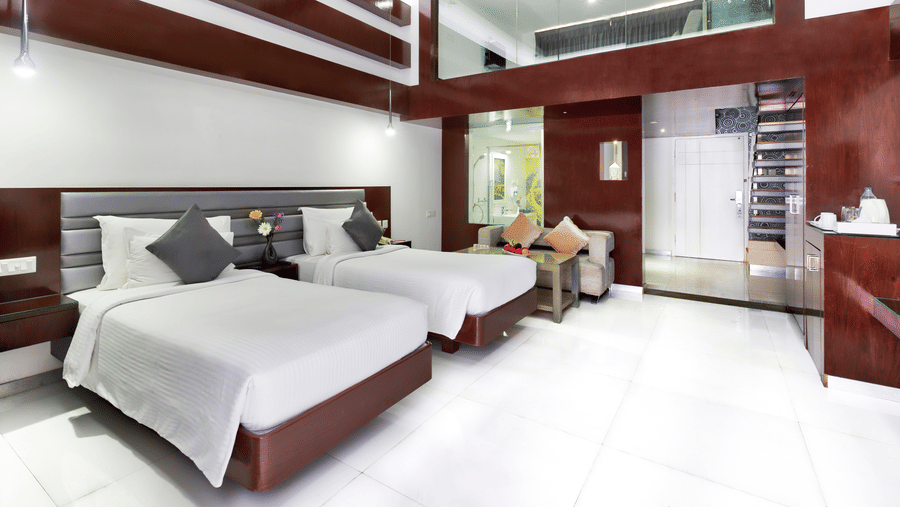 A clean hotel room featuring two beds with white linens, wooden accent walls, and a large window - Grande Bay Resort Booking in Mahabalipuram 