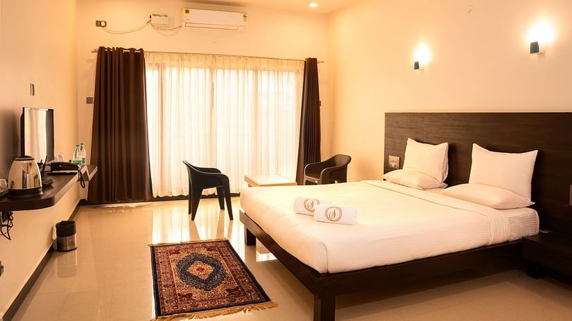 A deluxe ac room with a tv opposite a double bed at Mastiff Select Terrain, Dandel. The room also features a fan, a seating area with two chairs and a centre table, and a large window