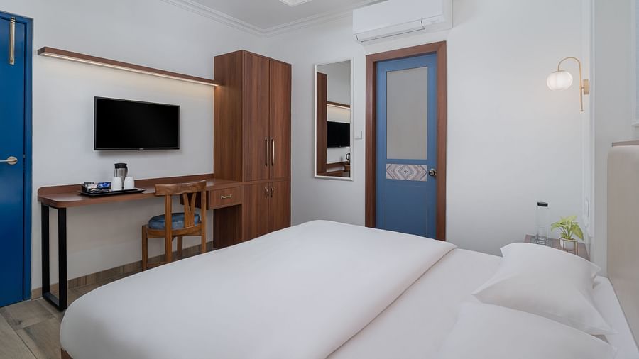 A spacious room featuring a large bed, a wall-mounted television above a wooden table, and a wooden cupboard next to it | Hotel Ganga Maiya