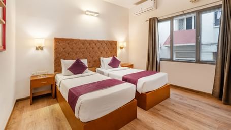 A hotel room with 2 single beds placed near a window with curtains opened– Monday Hotels HITEC City, Hyderabad