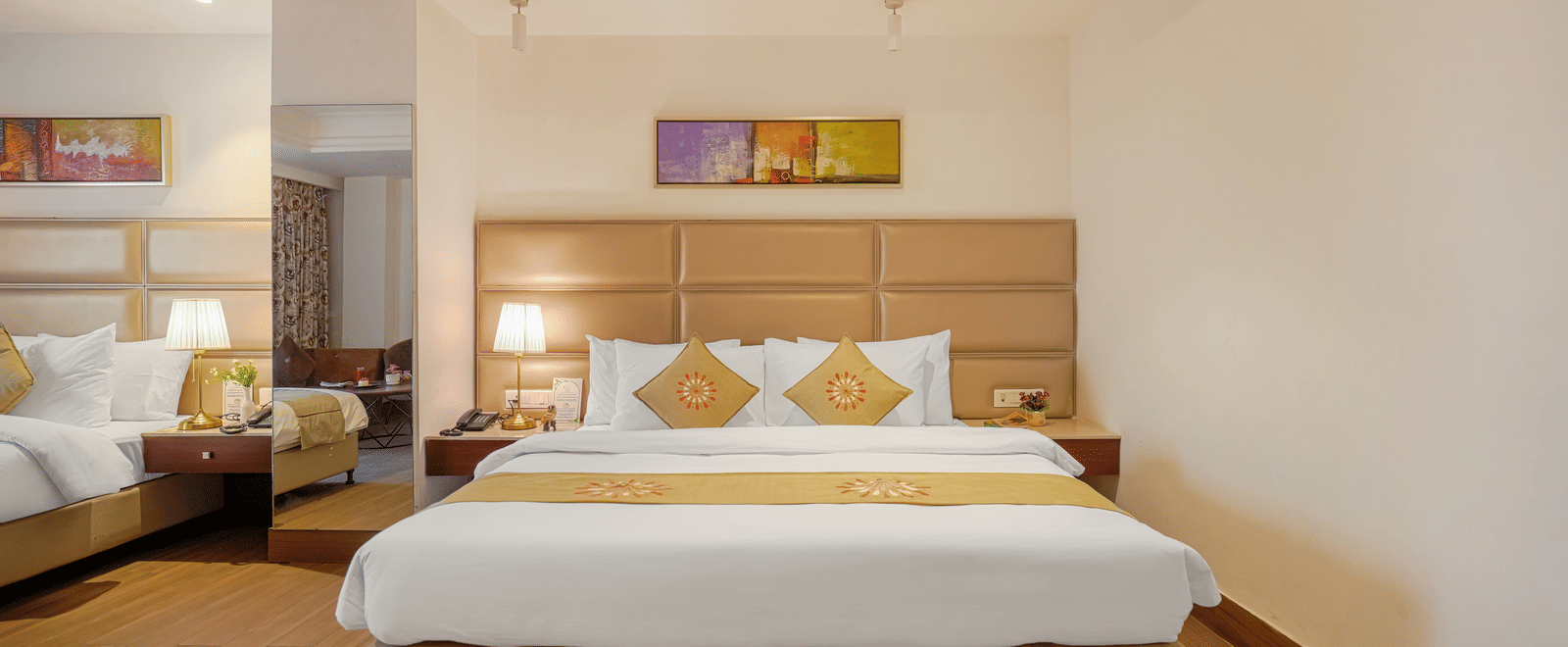 A view of an elegant hotel room featuring a large bed with a tan headboard, gold runner, and bright, white walls at BluSalzz Select City Centre, Amritsar.