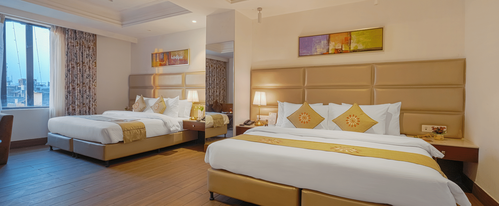 A wide-angle view of a hotel room with two large beds, bright lighting, and abstract artwork above the headboard at BluSalzz Select City Centre, Amritsar.