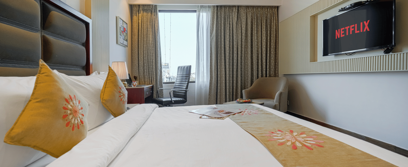 A hotel room featuring a large bed, a wall-mounted television, and a panoramic view of the city through a window at BluSalzz Select City Centre, Amritsar.
