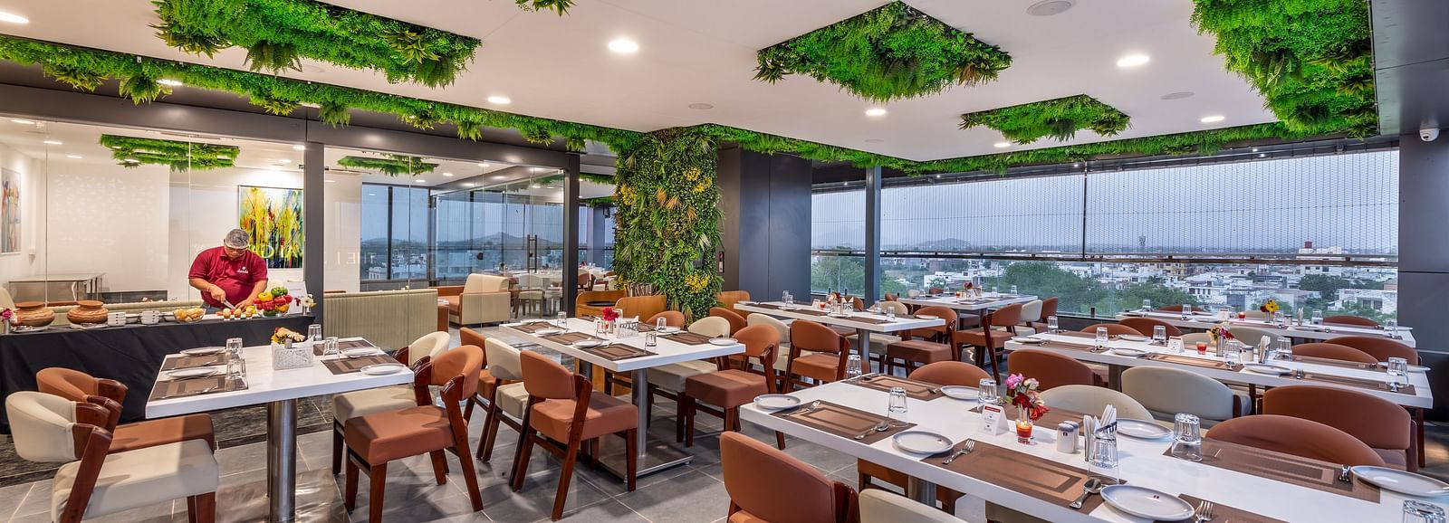 A stylish restaurant with large windows, chic furniture, and greenery lime tree on the ceiling.