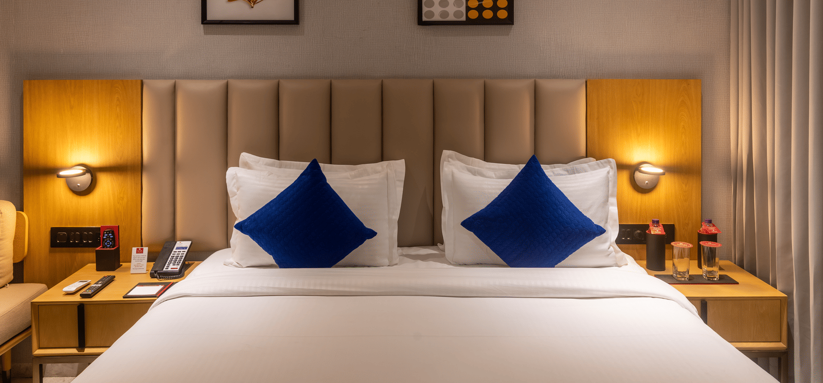 Cosy guest room with a plush bed, blue decorative pillows, warm ambient lighting, and wall art at Lords Studio Inn, Jamnagar