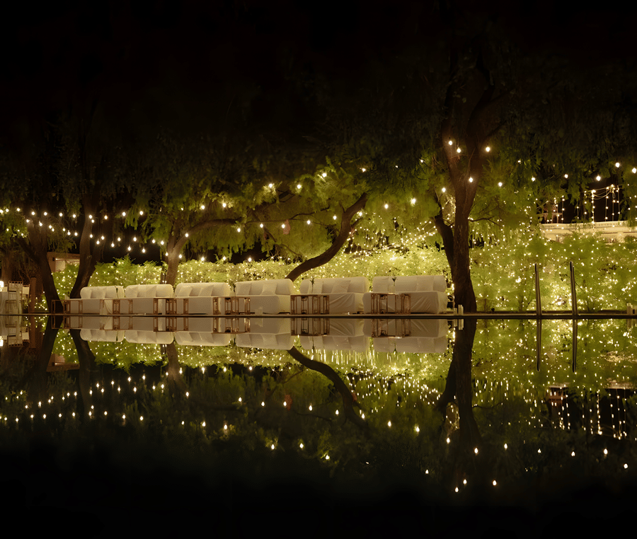 Evening decor with lights reflecting on water at Umaid Palace during Charvi & Dhruv wedding celebrations.
