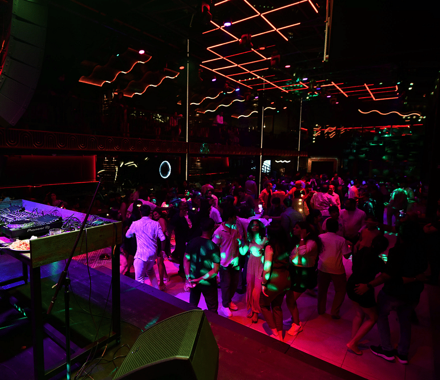 alt-text A DJ in a Hawaiian shirt spins tunes as the crowd dances beneath vibrant lights at Nysa Skybar, Bengaluru.