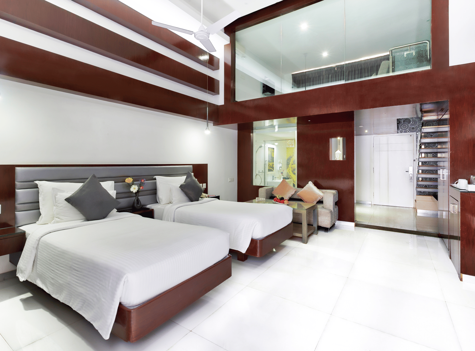 A clean hotel room featuring two beds with white linens, wooden accent walls, and a large window - Grande Bay Resort Booking in Mahabalipuram 