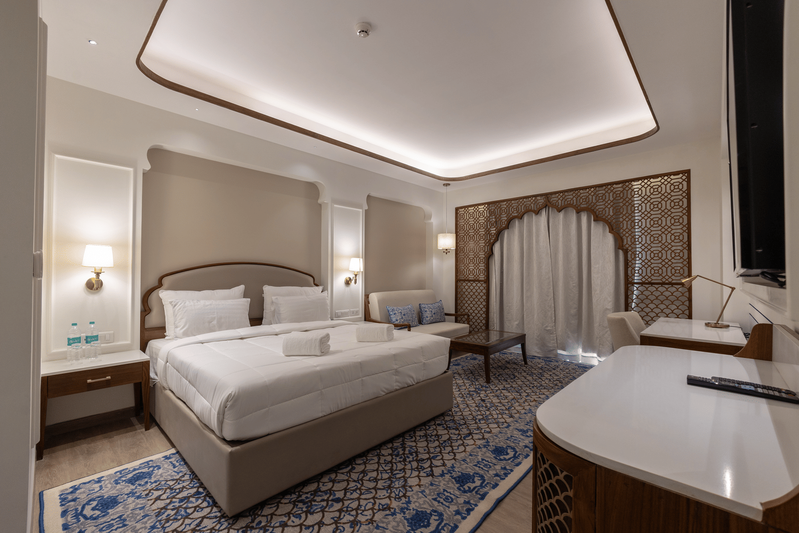 The bedroom of Jalrupa at Bhagirathi by Atishay featuring a large neatly made bed under warm lighting and a seating space by the window