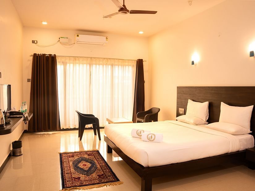 A deluxe ac room with a tv opposite a double bed at Mastiff Select Terrain, Dandel. The room also features a fan, a seating area with two chairs and a centre table, and a large window