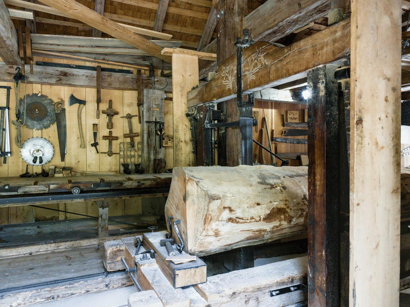 A woodworking machinery cutting a huge log inside a sawmill.